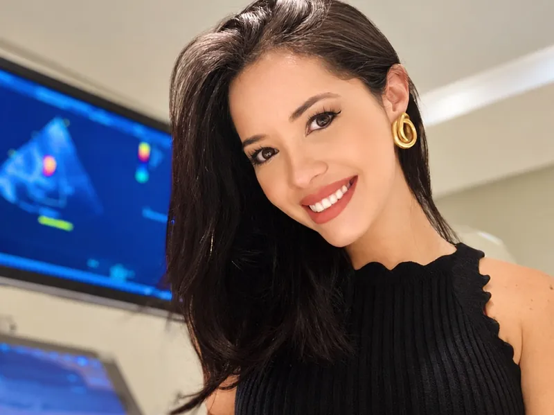 Dra. Alinne Barbosa em sua sala de atendimento com o ecocardiógrafo ao fundo