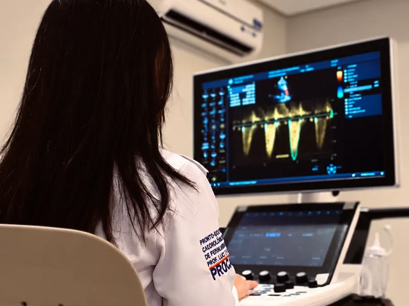 Dra. Alinne Barbosa de costas operando o ecocardiógrafo com imagem de Doppler na tela